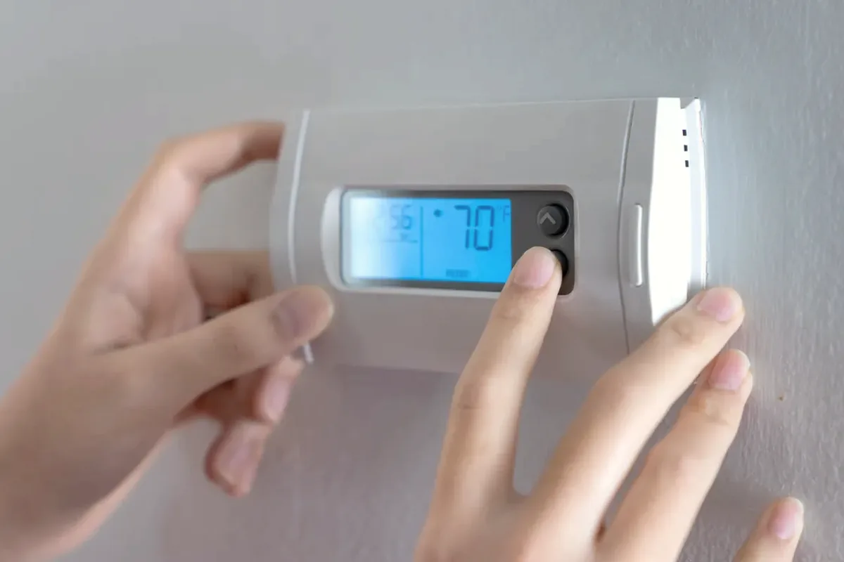 Hands adjusting a digital wall thermostat